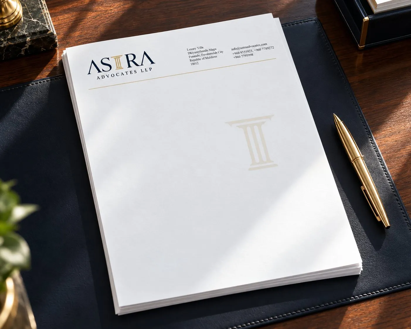 Astra Advocates LLP letterhead with a faint gold pillar watermark, on a navy desk pad beside a gold pen.