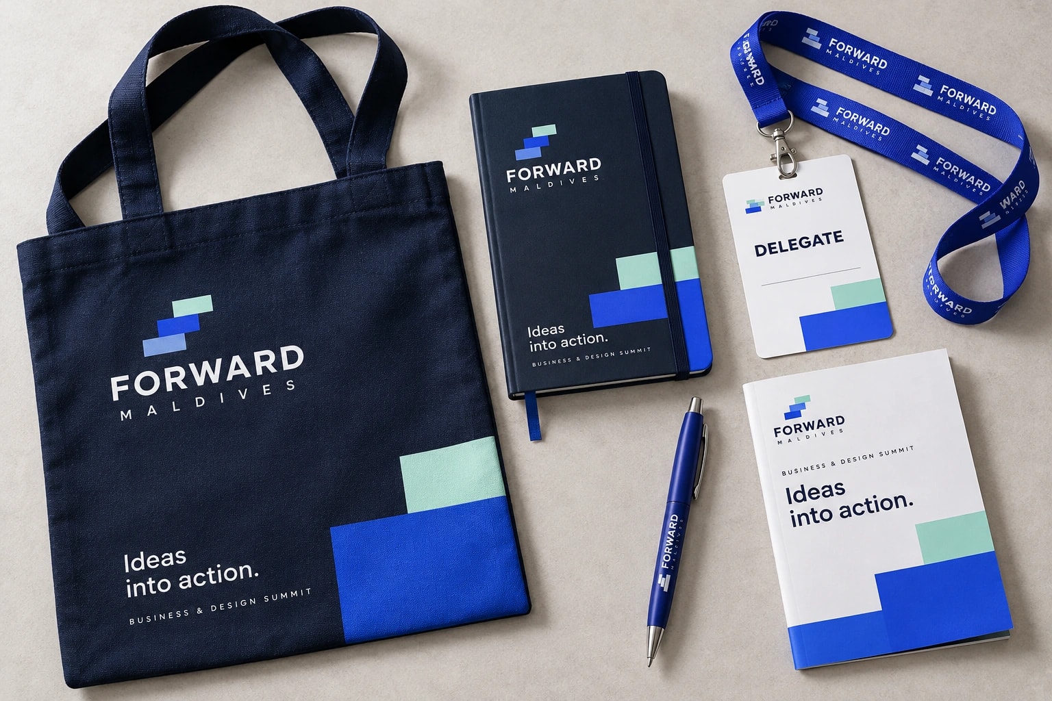 A navy Forward Maldives tote reading “Ideas into action.” sits with a matching notebook, pen, blue lanyard, delegate pass and white booklet on pale stone.