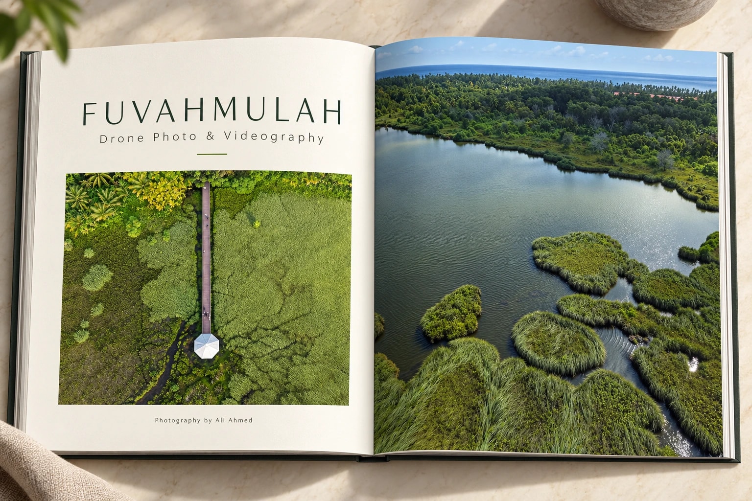 An open Fuvahmulah photo book with dark green capitals over a top-down wetland boardwalk, facing a full-bleed lake dotted with grassy islands.