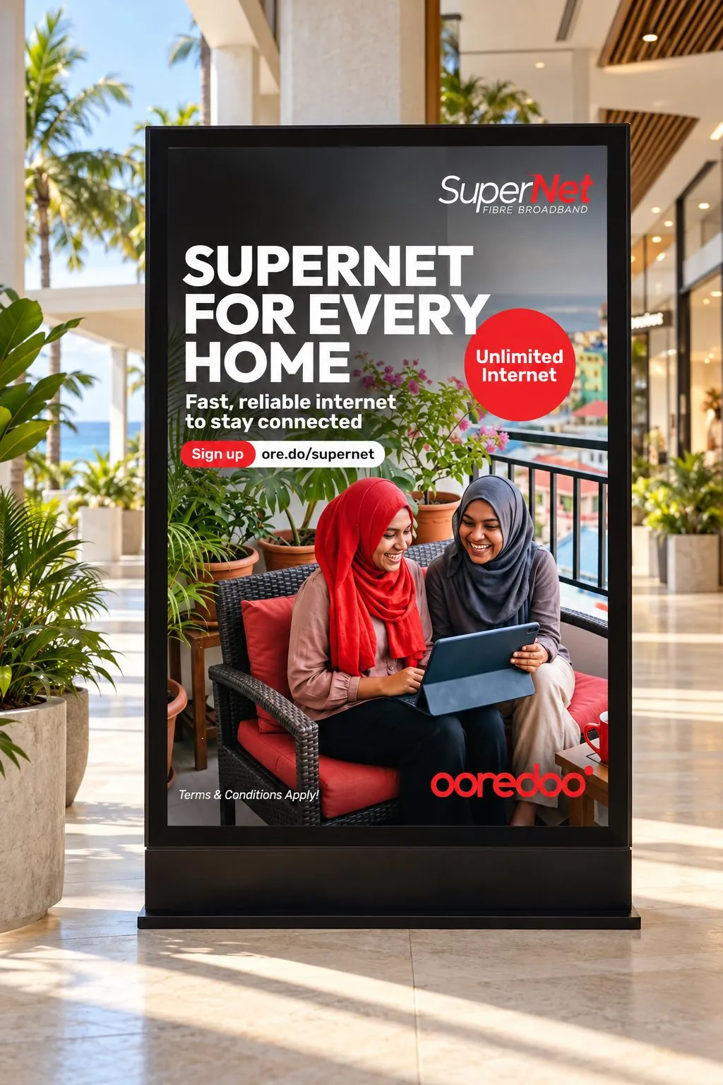 SuperNet poster, “Supernet for every home”, with two women sharing a tablet on a sofa, in a display stand in a mall.