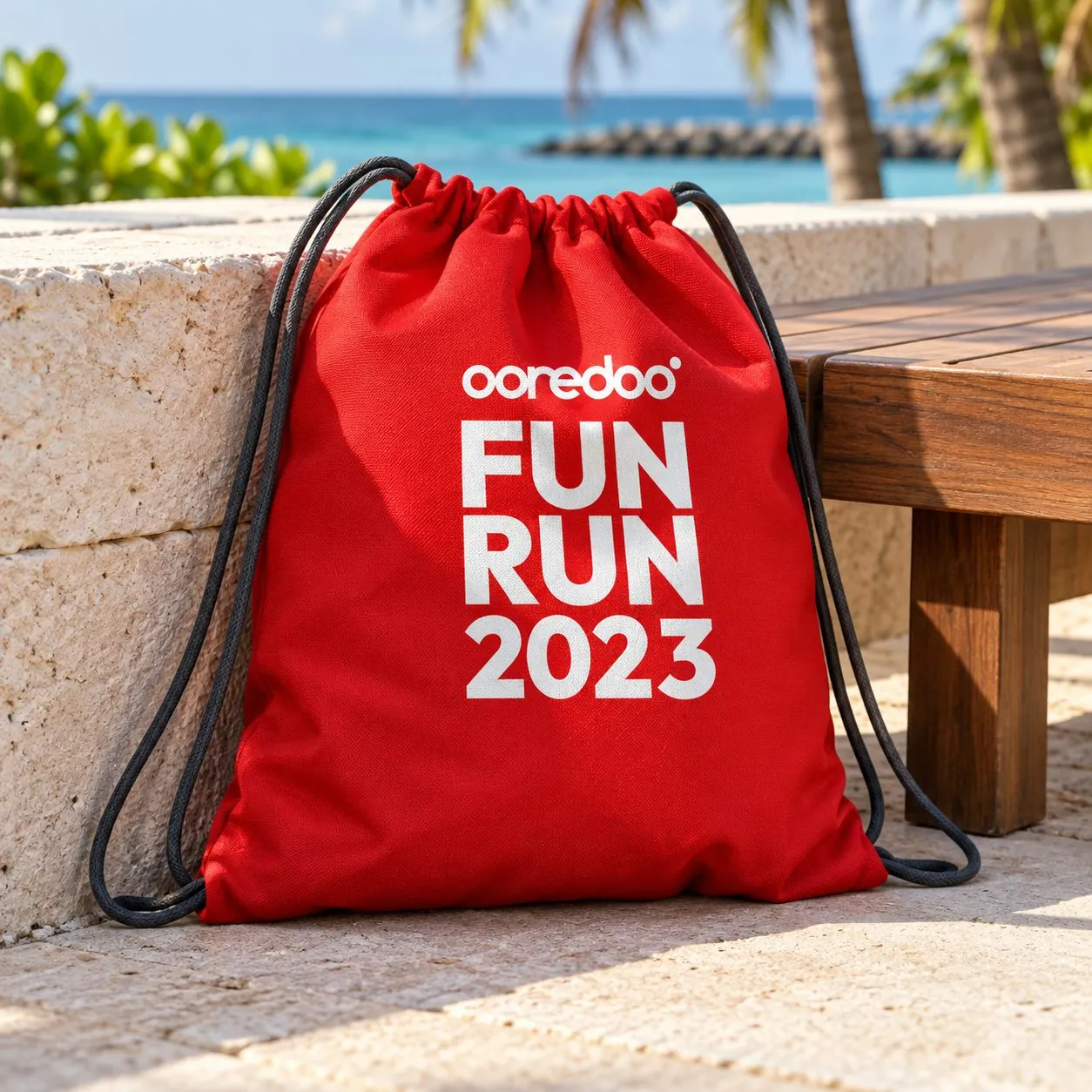 Red Ooredoo Fun Run 2023 drawstring bag propped on a stone ledge by the beach.