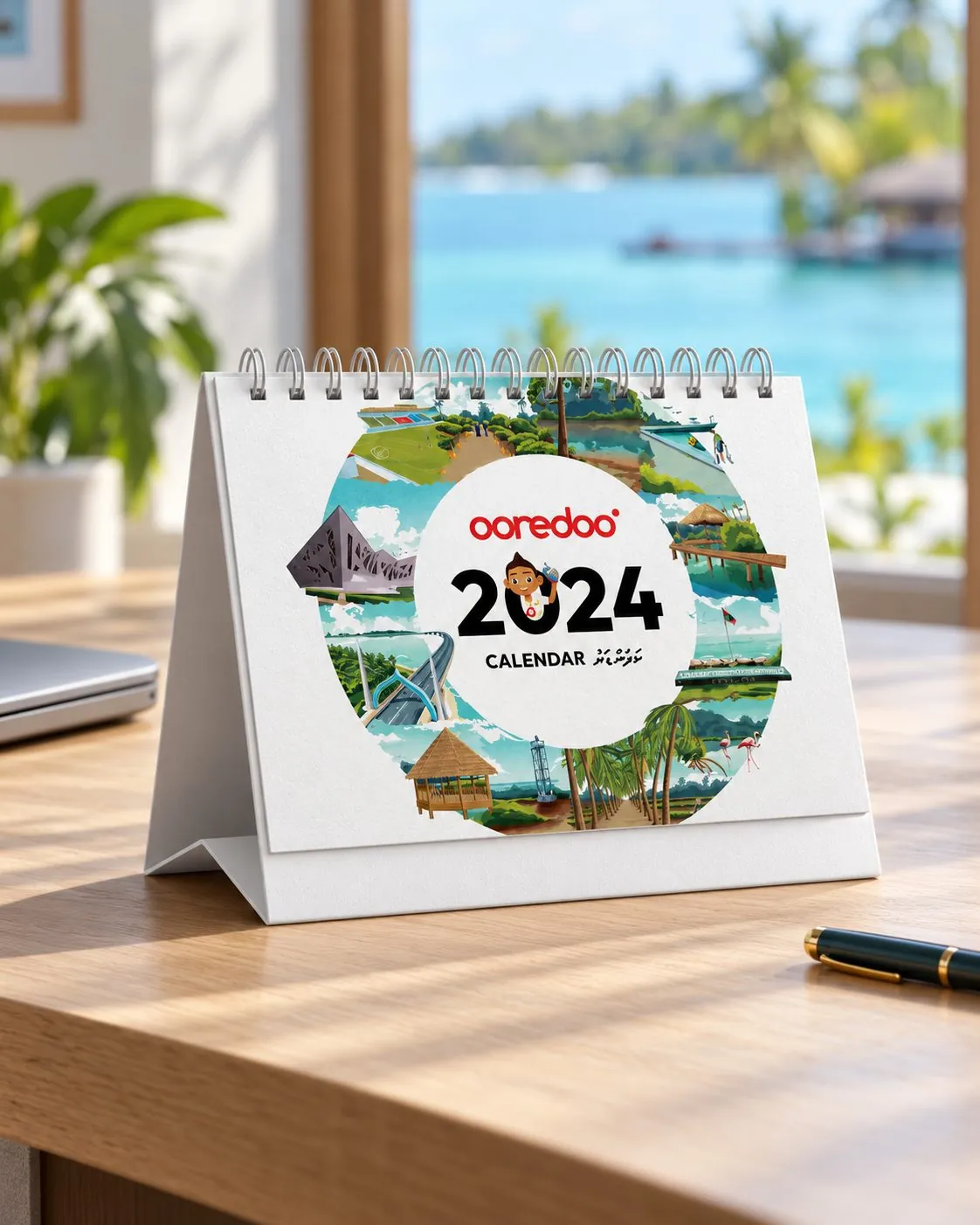 Ooredoo 2024 desk calendar with a ring of Maldives scenes around the year, on a desk by a window.