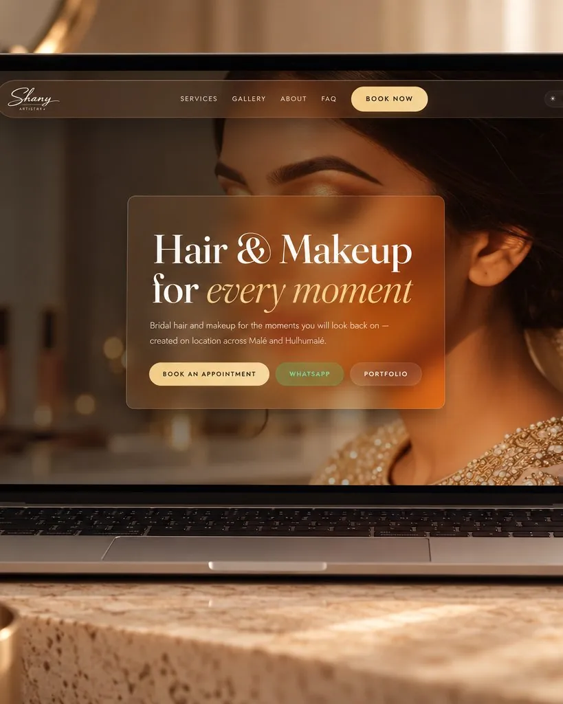 Shany Artistry home page, “Hair & Makeup for every moment”, in gold glass over a bridal portrait, on a laptop.