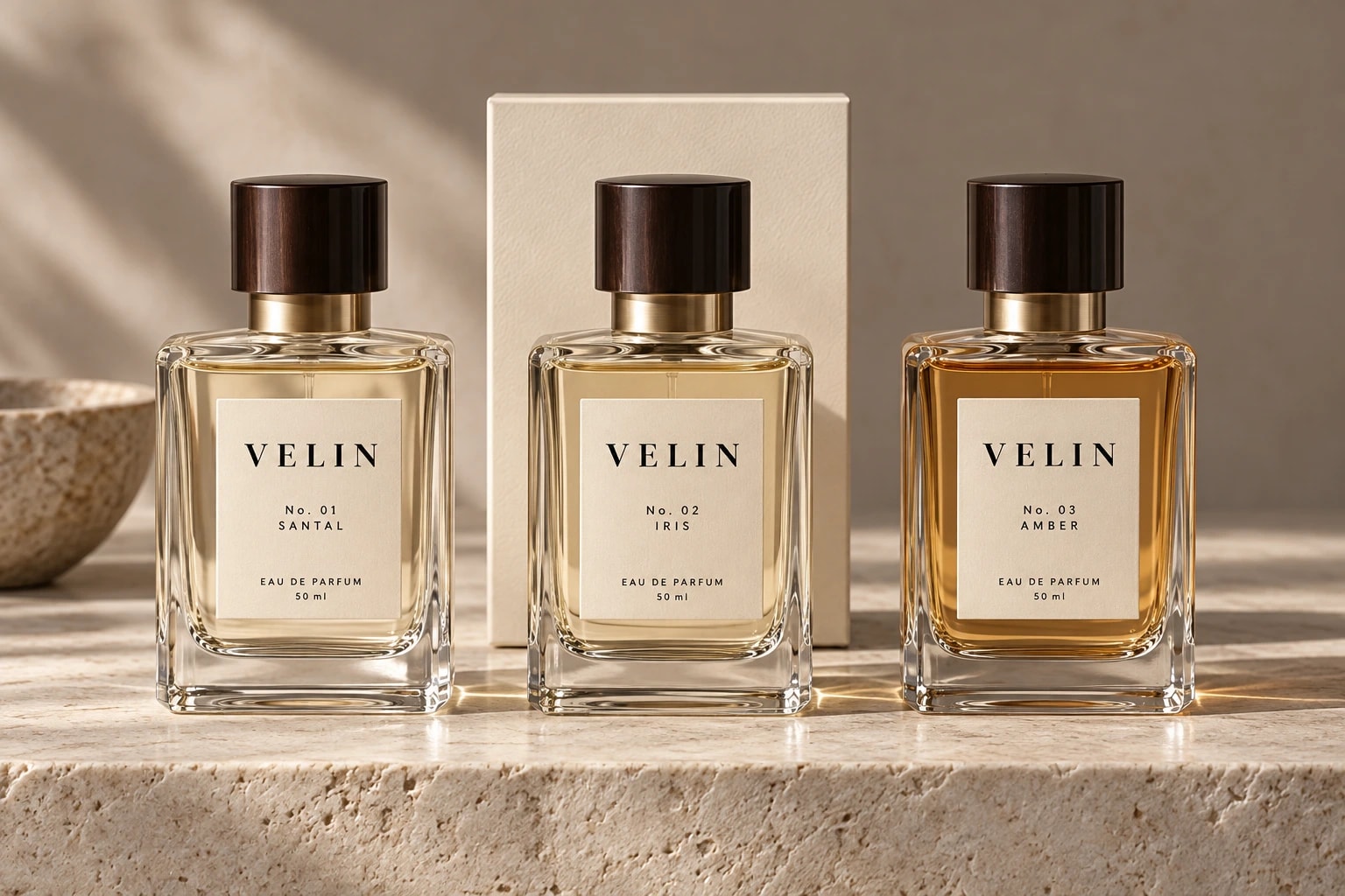 Three Velin bottles, “No. 01 SANTAL”, “No. 02 IRIS” and “No. 03 AMBER”, in a row before a cream box on a pale stone ledge.