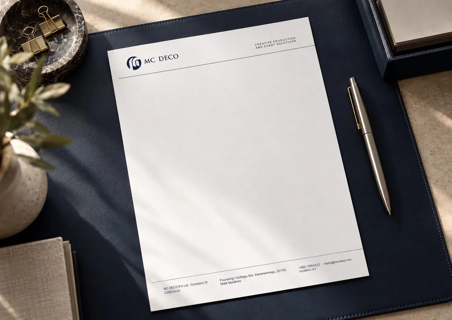 MC Deco letterhead with the arch monogram, on a navy leather desk pad beside a silver pen.