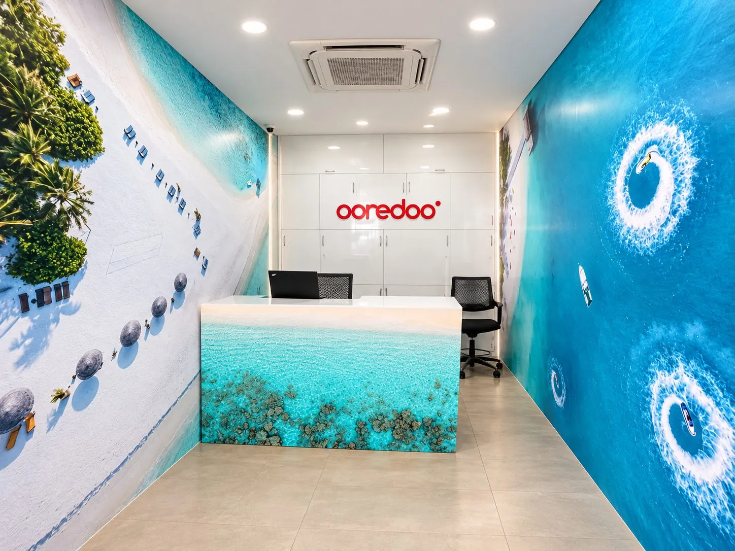 Ooredoo customer counter with a lagoon printed on the desk and aerial sea and beach murals across the walls.
